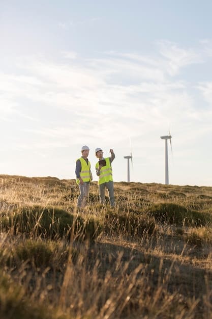 A group of workers constructing a new wind turbine on a grassy hill, with a clear blue sky and fluffy clouds in the background.