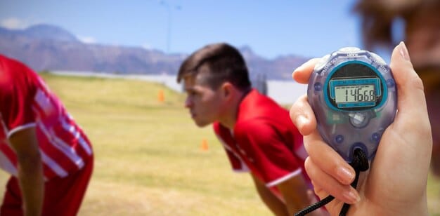 An image of a pitching coach holding a stopwatch, timing a pitcher's delivery during practice. This image emphasizes the data-driven approach and strategic adjustments teams are making to comply with the pitch clock.