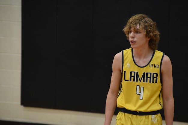 A close-up of a college basketball player, wearing a jersey with a blurred background of a different team's stadium, symbolizing his recent transfer. The image conveys a sense of transition and new beginnings.