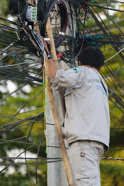 A technician installing fiber optic cables in a rural area. The background shows farms and open fields, highlighting the focus on expanding broadband to underserved regions.